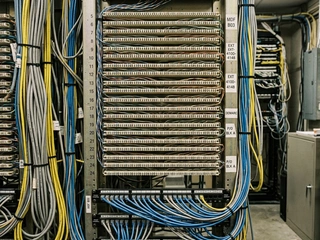 Telephone patch panel or distribution frame in a communications room; representing the physical telephone infrastructure that monitoring centres had to manage