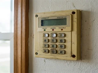 Worn alarm system keypad showing physical degradation from years of daily use; a visual indicator of system age