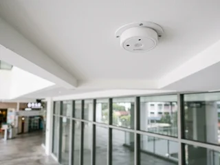 Glass break acoustic sensor mounted on a wall near a large glazed window in a commercial Singapore interior