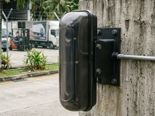 Outdoor perimeter photobeam sensor pair mounted on posts at a Singapore car park or compound perimeter